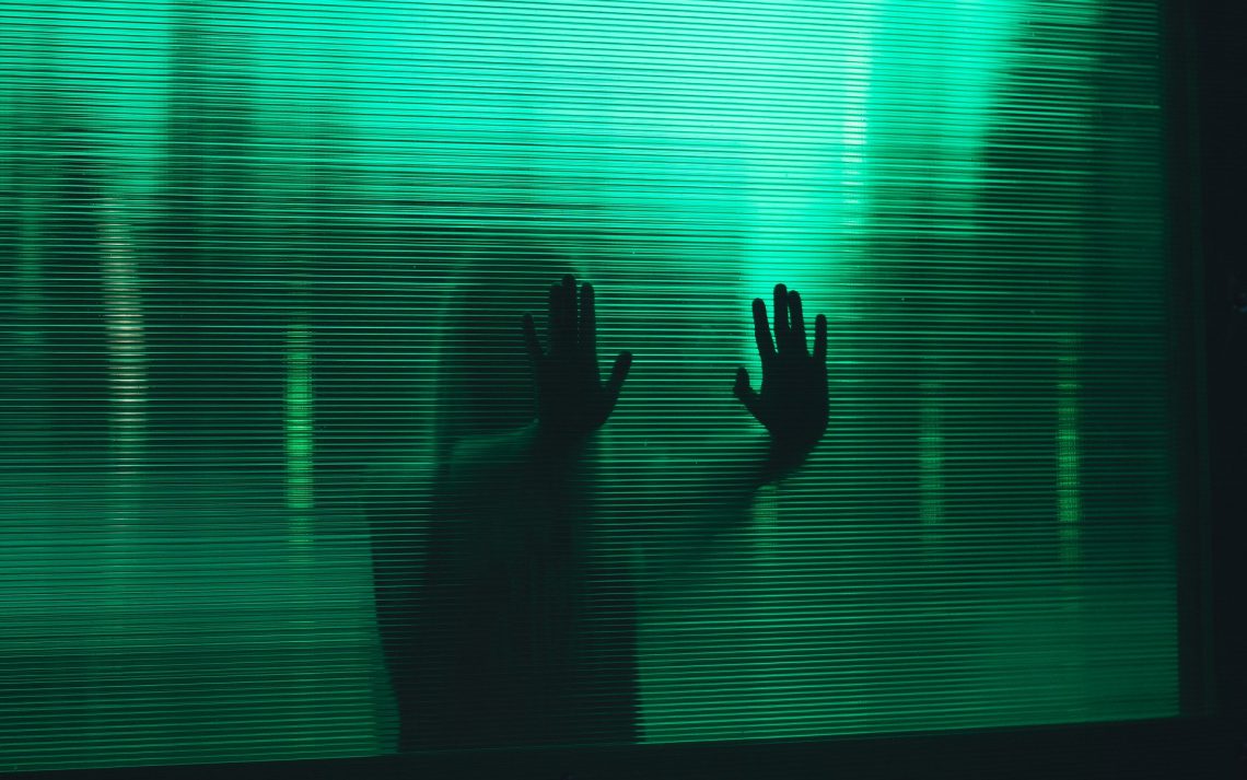 Eine Person hält ihre Hände gegen eine grüne Glaswand