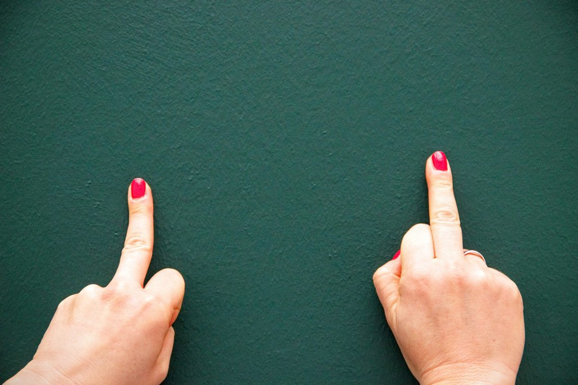 Zwei Stinkefinger, mit rot lackierten Fingernägeln, vor grünem Hintergrund.